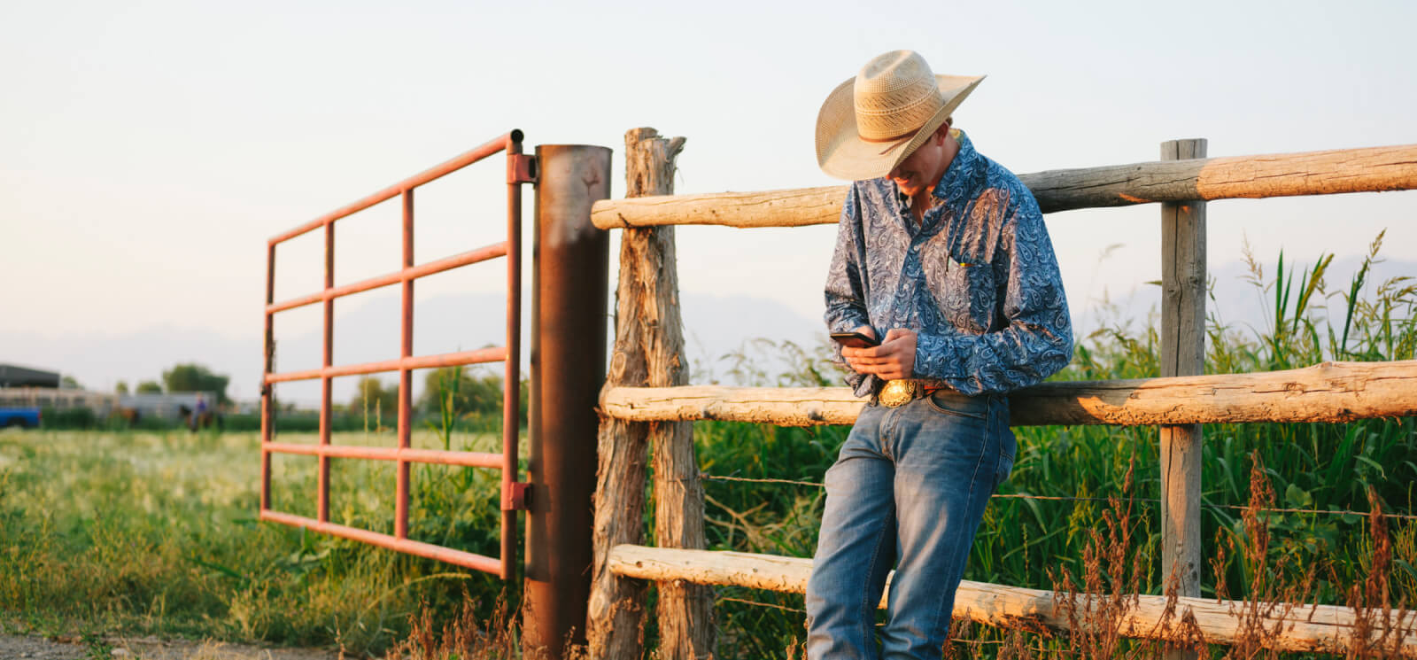 Man in cowboy cat in a field looking at a smartphone